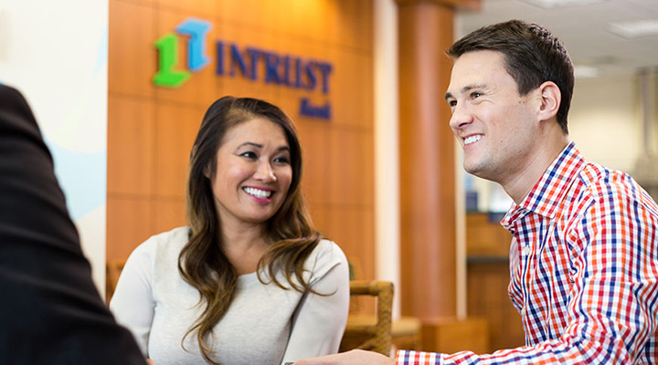 A young man and woman smile while sitting at a desk in an INTRUST banking center